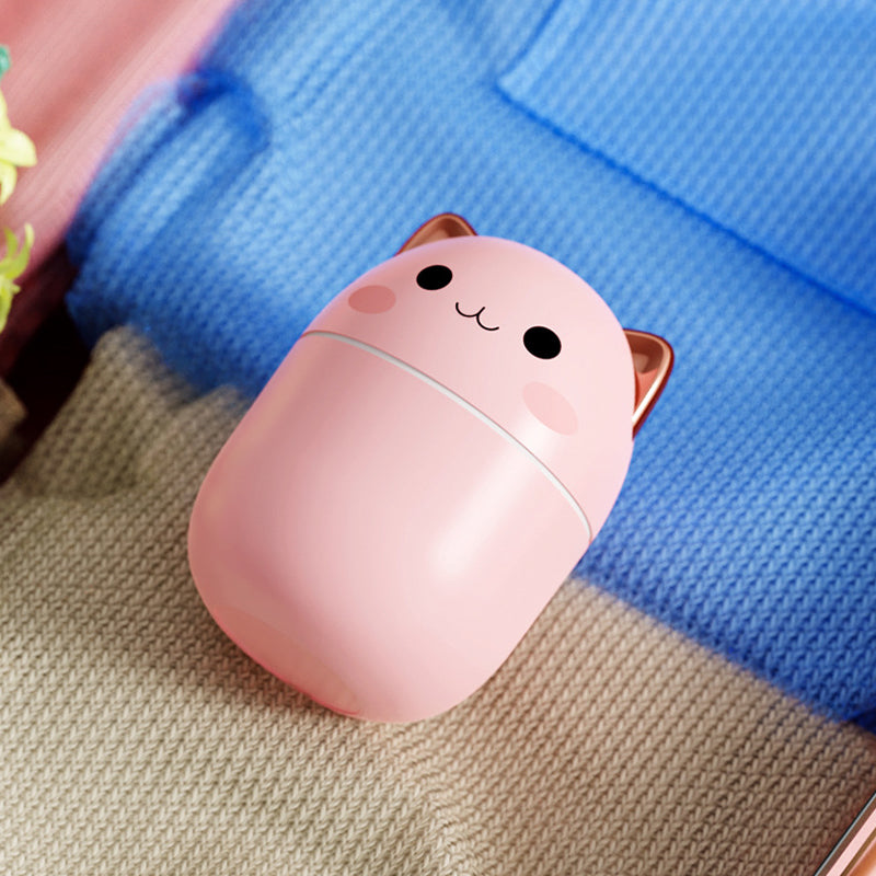 Cute pink cat-shaped compact mirror on a textured surface with a blue fabric background