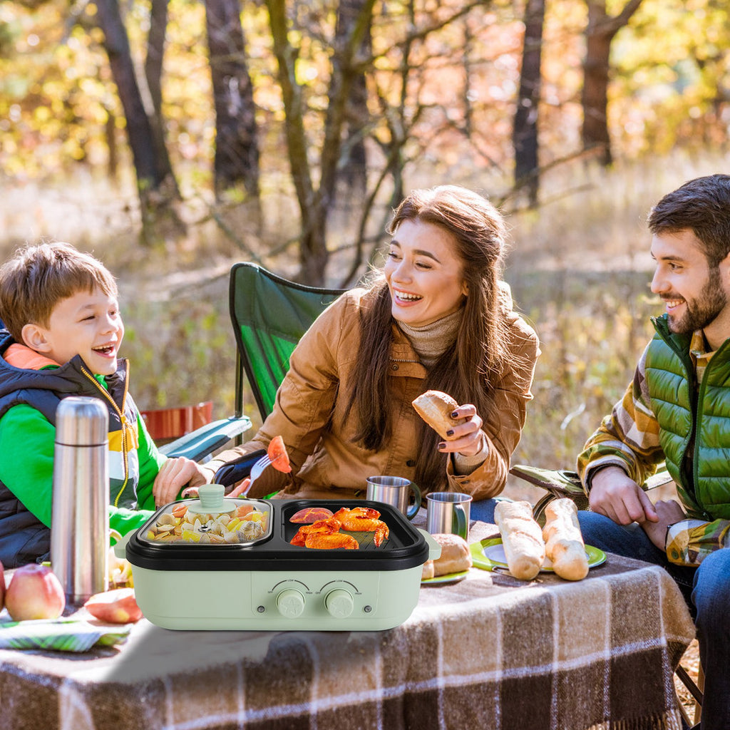 Family of four enjoying a picnic outdoors with a portable grill on a checkered blanket.