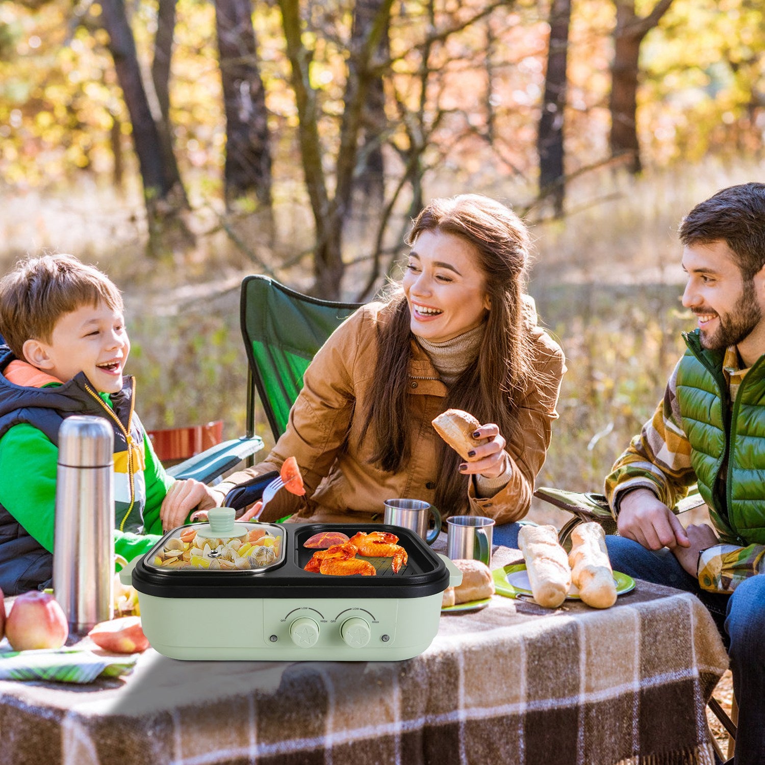 Family of four enjoying a picnic outdoors with a portable grill on a checkered blanket.